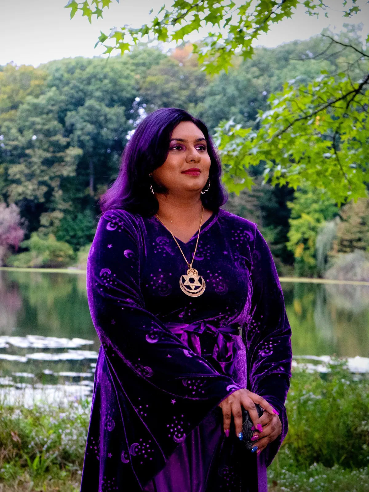 Ashley Ali in a purple velvet moon-and-star dress beside a lake