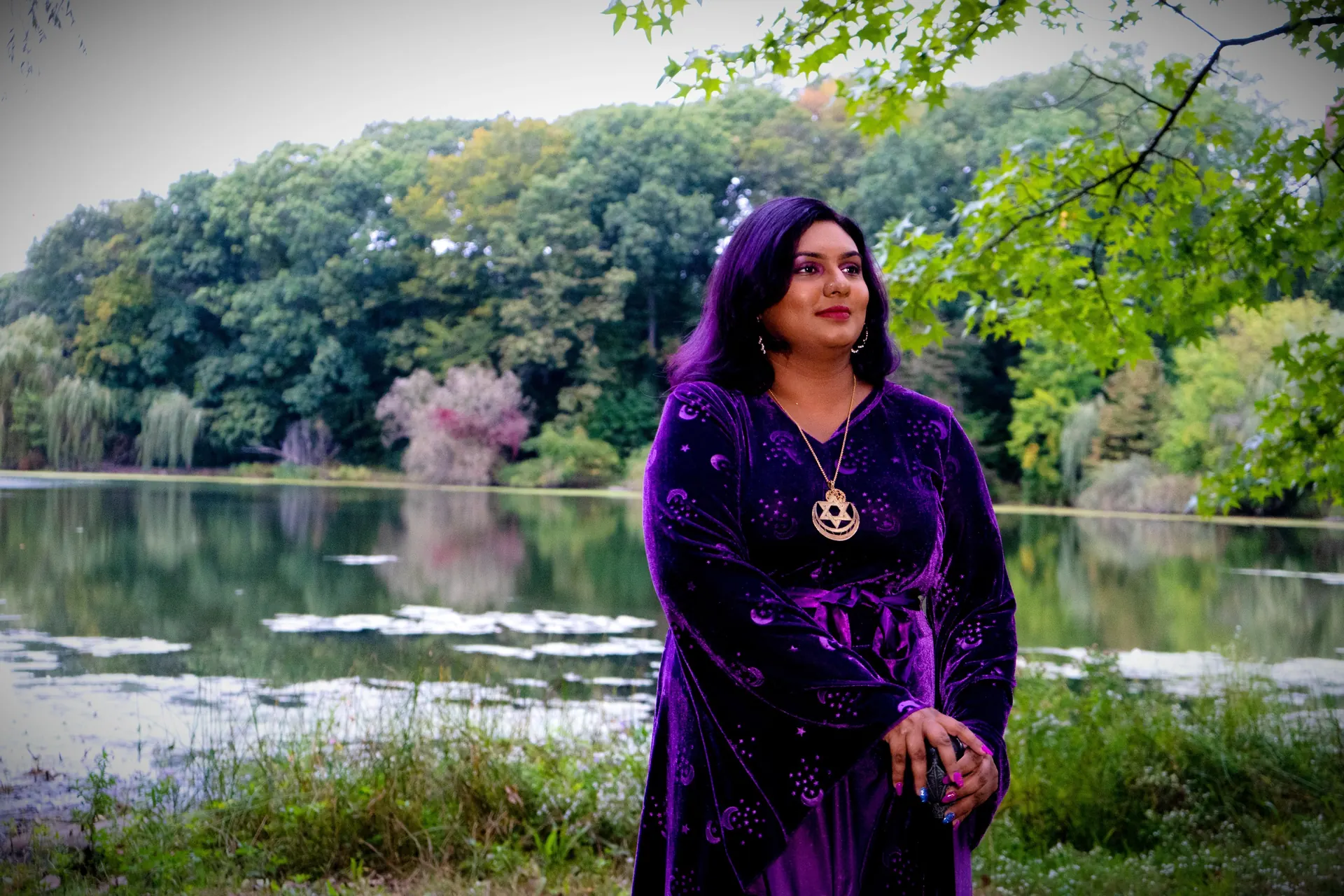 Ashley Ali in a purple velvet dress by a lake surrounded by trees