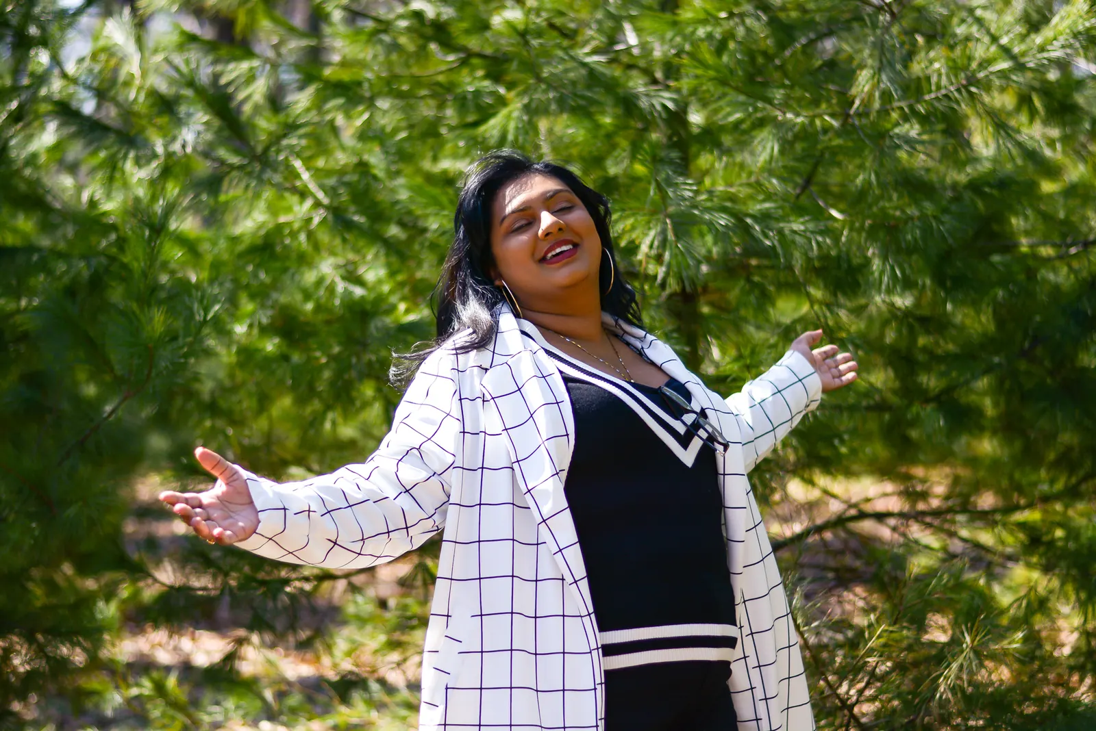 Ashley Ali smiling with arms wide open among pine trees