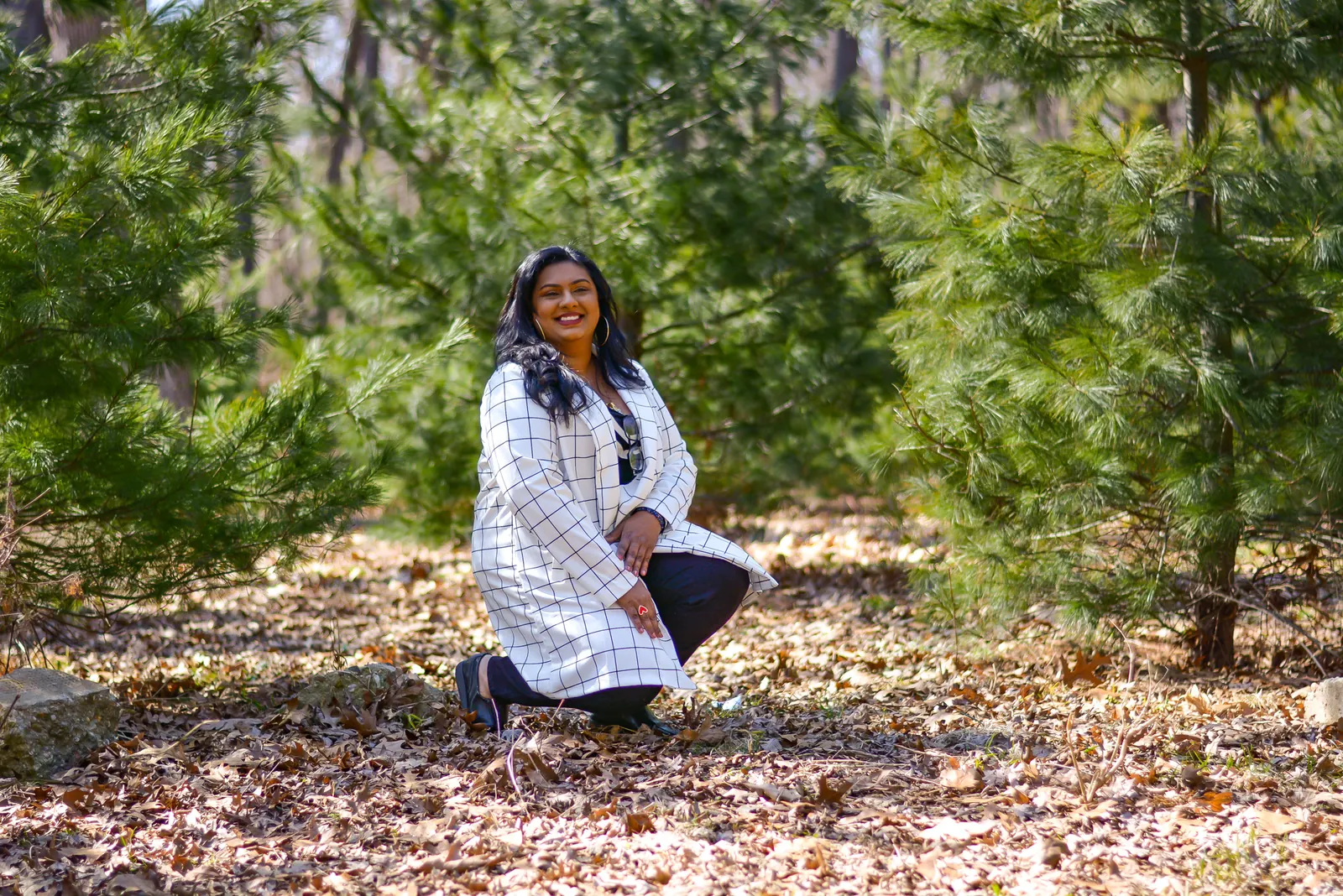 Ashley Ali kneeling among pine trees on autumn leaves
